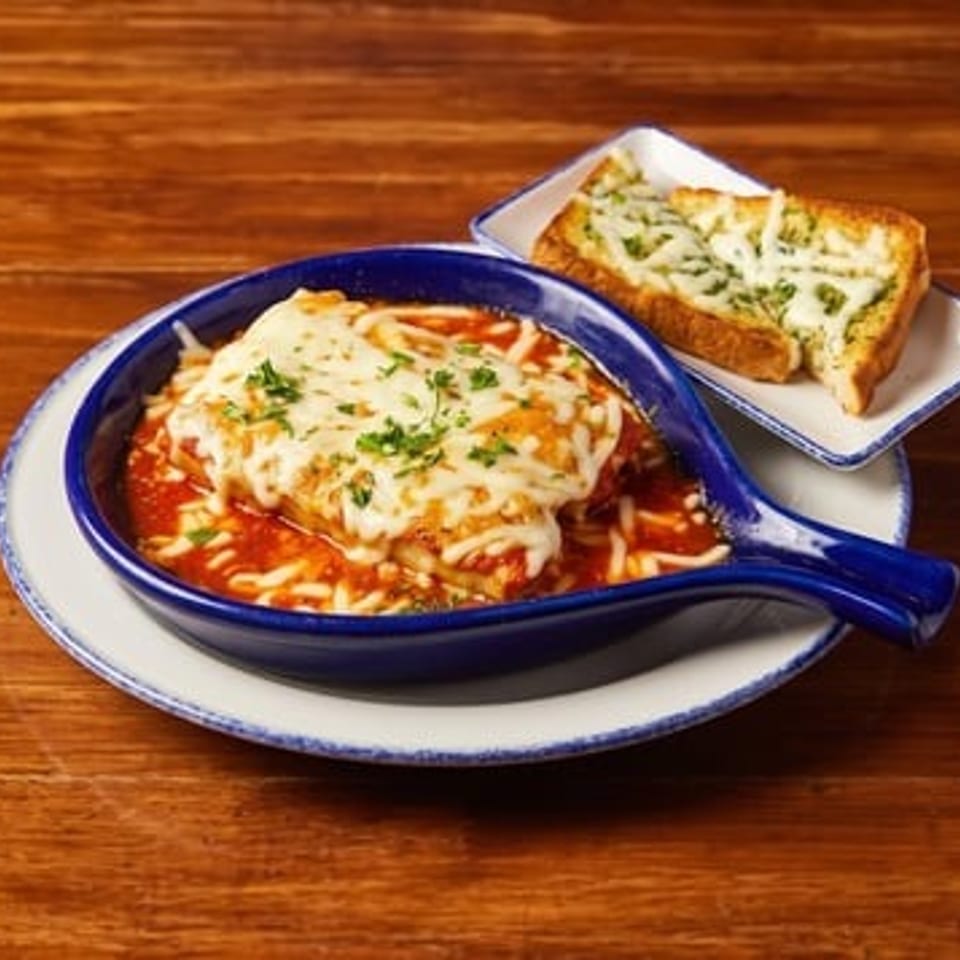 Cheesy baked lasagna in a blue skillet with marinara sauce, served alongside garlic bread on a wooden table.