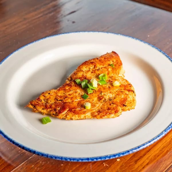 Grilled chicken breast seasoned with herbs and topped with chopped green onions on a white plate.