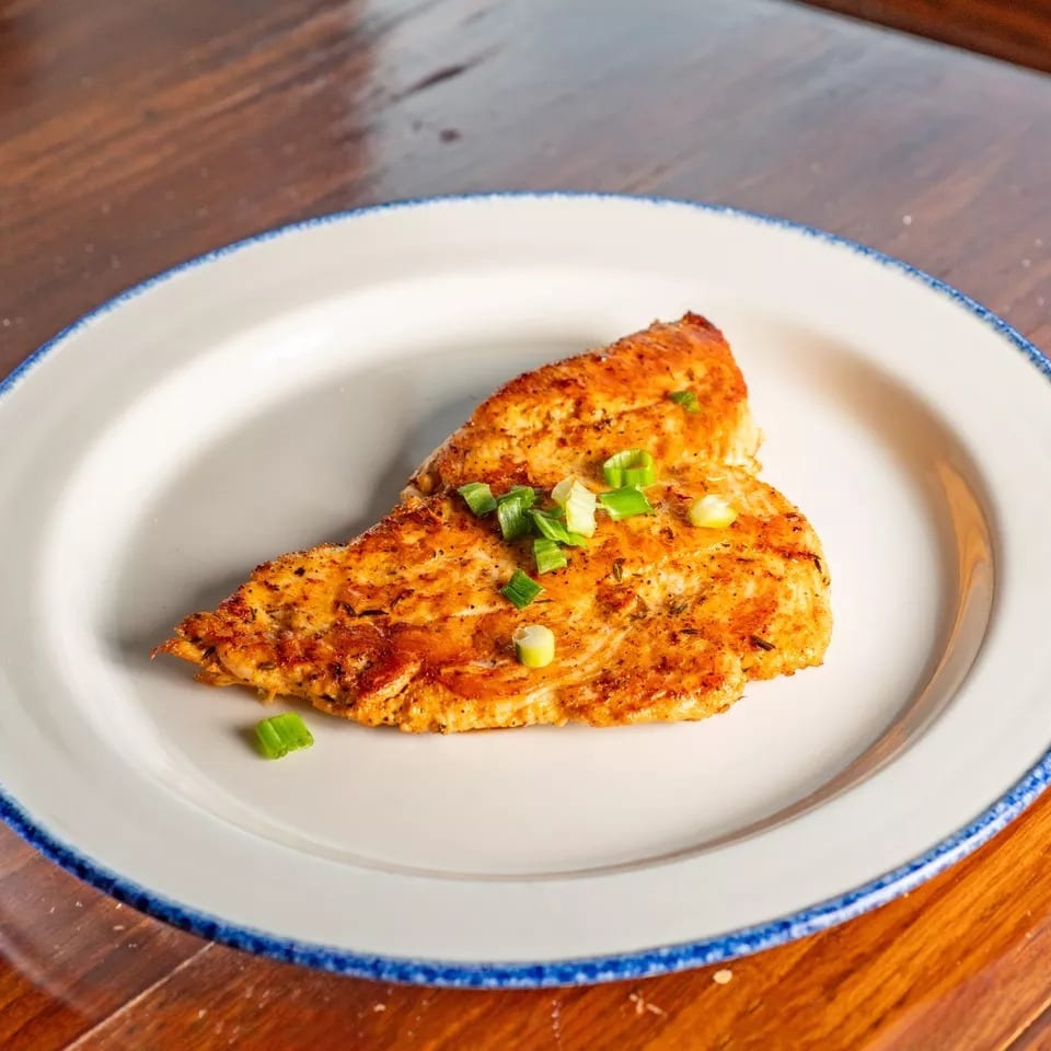 Grilled chicken breast seasoned with herbs and topped with chopped green onions on a white plate.