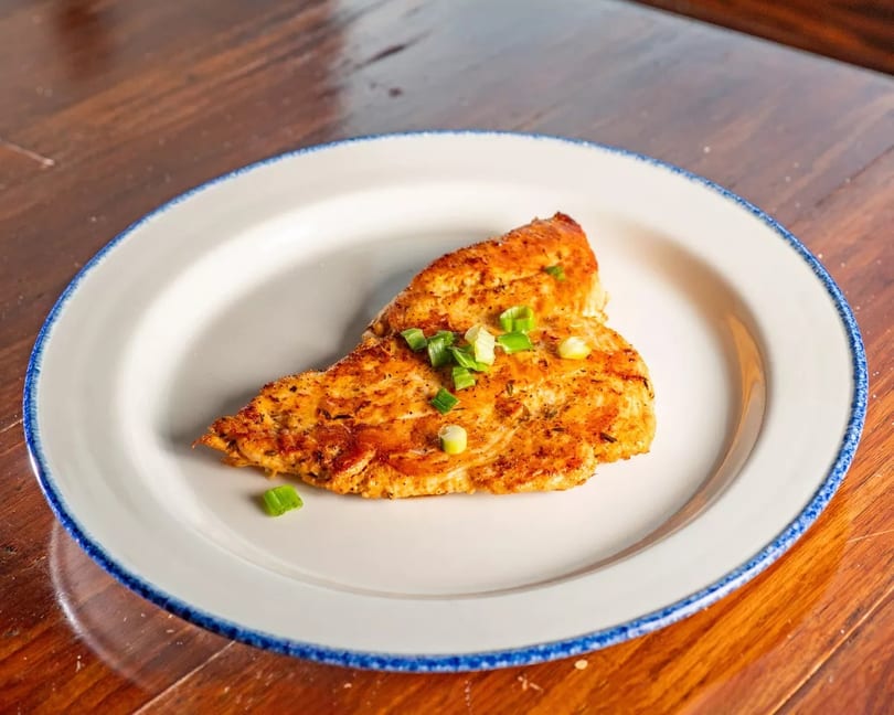 Grilled chicken breast seasoned with herbs and topped with chopped green onions on a white plate.