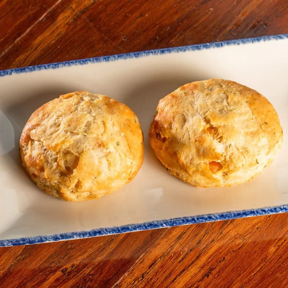 Two golden-brown biscuits with herbs on a white rectangular plate with a blue rim, on a wooden table.