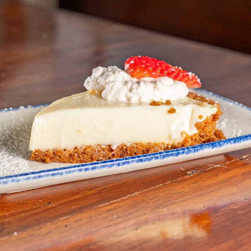 A slice of key lime pie with whipped cream and a strawberry on a white and blue plate.