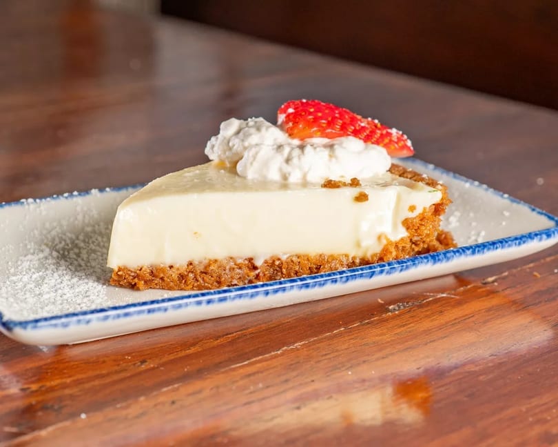 A slice of key lime pie with whipped cream and a strawberry on a white and blue plate.