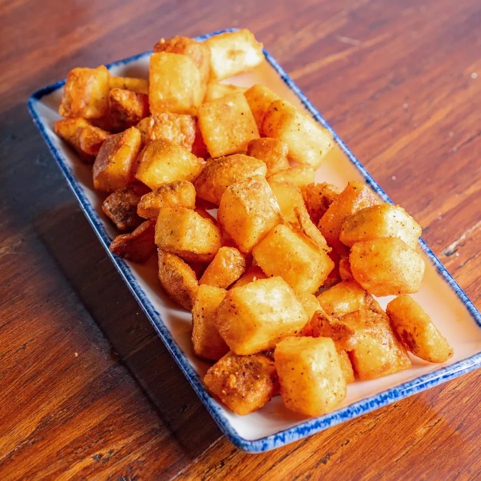 Crispy golden-brown fried potatoes seasoned with spices, served on a rectangular white plate with blue trim.