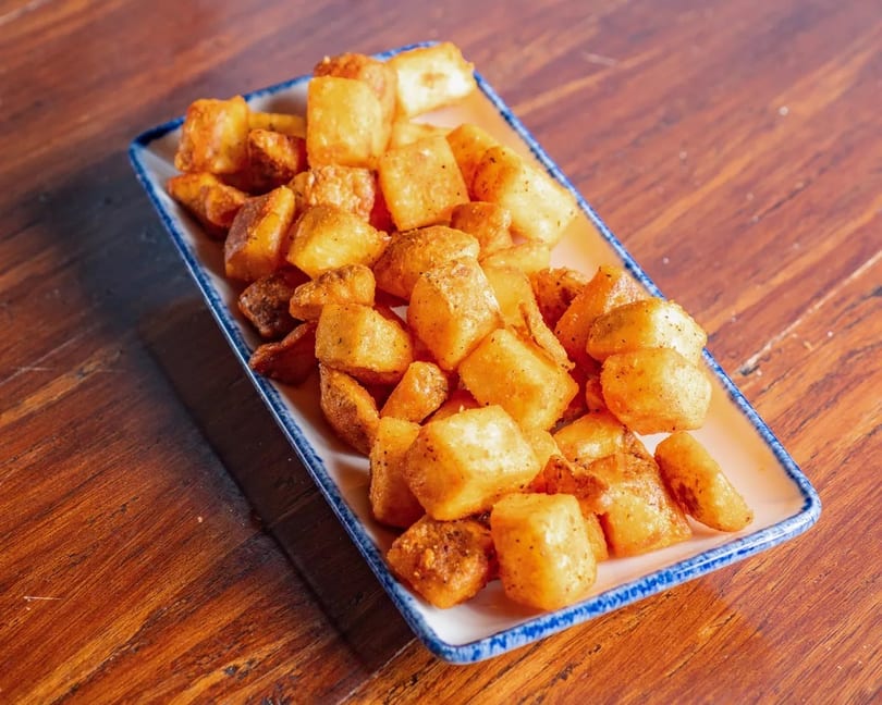 Crispy golden-brown fried potatoes seasoned with spices, served on a rectangular white plate with blue trim.