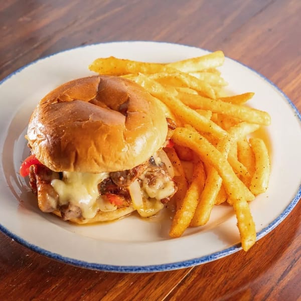 Cheesesteak sandwich with melted cheese, onions, and peppers, served with golden french fries.