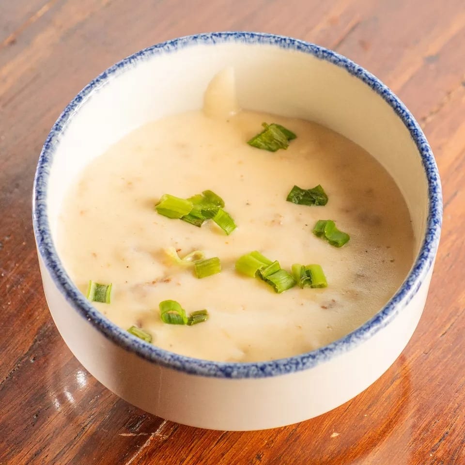 Creamy soup topped with chopped green onions in a white bowl with a blue rim on a wooden table.