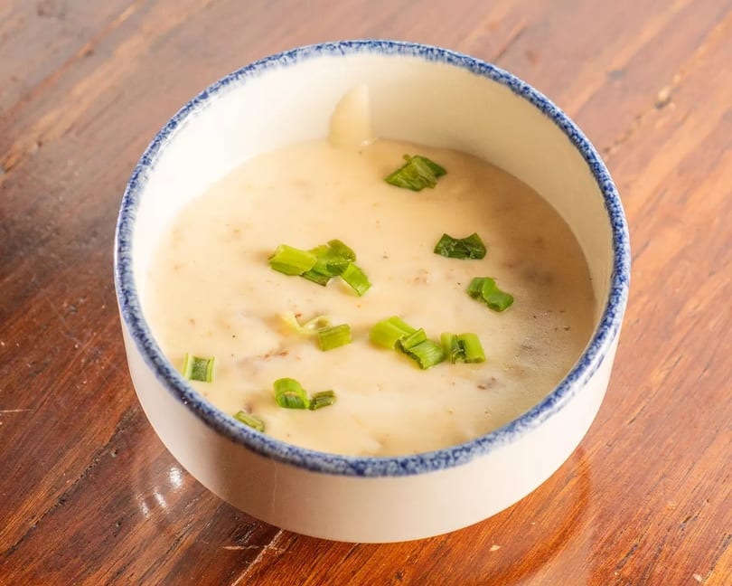 Creamy soup topped with chopped green onions in a white bowl with a blue rim on a wooden table.