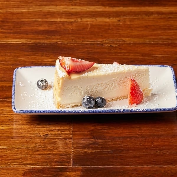 A slice of cheesecake with strawberries and blueberries on a white rectangular plate.